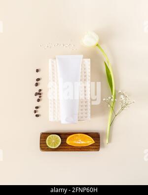 Composizione verticale con tubo cosmetico su un asciugamano bianco, tulipano, arancio, laim e chicchi di caffè. Il concetto di prodotti naturali per la cura della pelle realizzati con e. Foto Stock