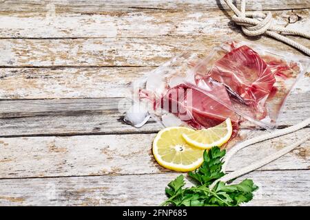 Filetti di tonno rosso in confezione sottovuoto su fondo di legno grigio. Pesce fresco, limone e prezzemolo per cucinare gli ingredienti. Concetto di alimentazione sana. Protei Foto Stock
