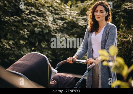 Donna che spinge un passeggino e guarda il suo bambino. Madre che prende il suo bambino fuori in un pRAM. Foto Stock