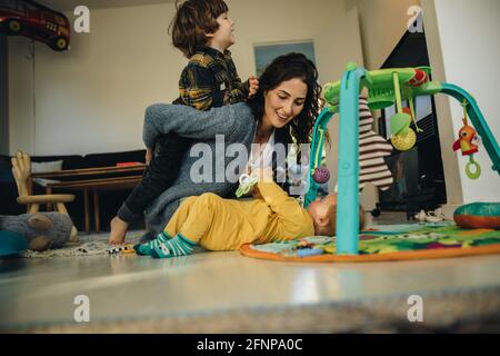 Donna che gioca con i suoi figli a casa. Madre che si prende cura dei suoi due bambini a casa. Foto Stock