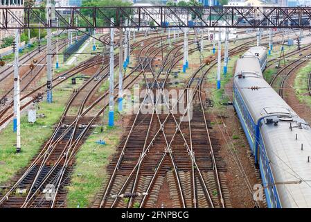 Ampia rete ferroviaria multicanale per treni in primavera, carrozze blu di un treno in partenza, ritmo delle rotaie, vista dall'alto. Foto Stock