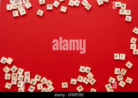 Immagine di sfondo le lettere sono sparse in disordine. Lettere inglesi. Lettere quadrate di legno su sfondo rosso brillante. Biglietto d'auguri, pronto all'uso Foto Stock