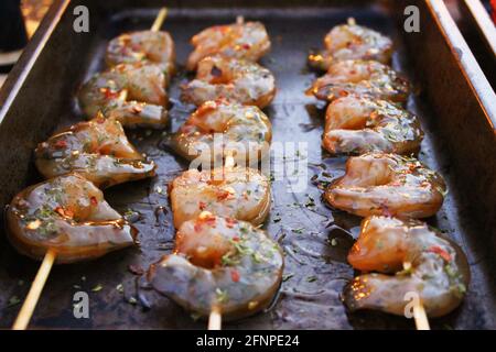 Primo piano di gamberetti stagionati e marinati su spiedini, in una padella con olio d'oliva. Foto Stock