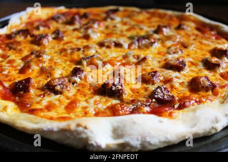 Primo piano di pizza appena sfornata fatta in casa, ancora in padella, su tagliere di legno. Foto Stock