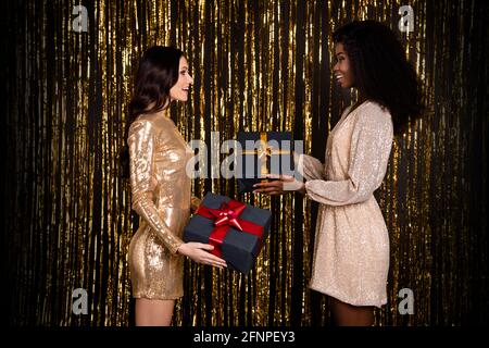 Foto di due donne di classe eccitato scambio regali tenere scatole indossa un abito lucido con fondo in tinsel isolato Foto Stock