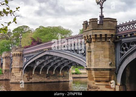 Un ponte storico in pietra con decorazioni in metallo e torri si estendono su un fiume. Gli alberi sono sullo sfondo e un cielo nuvoloso è sopra. Foto Stock