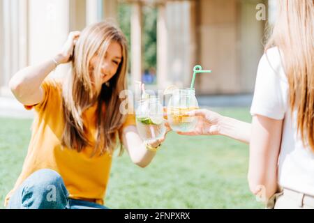 Due donne che si siedono sull'erba con cocktail alla limonata. Foto Stock