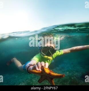 Foto subacquea di un ragazzo adolescente snorkeling con immersione Maschera di faccia nelle onde blu dell'Oceano Indiano vicino a. Isola di Zanzibar con un grande starbi arancione Foto Stock