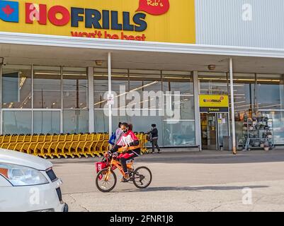 Toronto, Canada, 2021 maggio - giovane ragazza nera di consegna che indossa la maschera facciale sulla bicicletta di fronte ad un negozio di alimentari Foto Stock