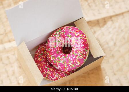 Due ciambelle rosa smaltate in primo piano in scatola di carta. Vista dall'alto. Dolci. Vendita, acquisto, consegna di prodotti freschi da forno, negozio online Foto Stock