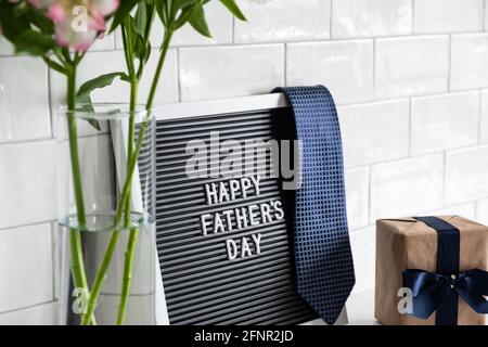 Concetto di Giornata dei Padri felici. Tavola da lettera, cravatta da collo, confezione regalo, boquet di fiori sul tavolo. Tessere sullo sfondo Foto Stock