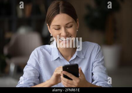 Una giovane donna positiva ama navigare sul Web al telefono in ufficio Foto Stock