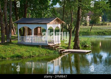 Gazebo estivo sulla riva dello stagno. Pergola di legno a Merechevshchina, luogo di nascita di Tadeusz Kosciuszko, vicino al villaggio di Kossovo Brest regione, Bielorussia. Foto Stock