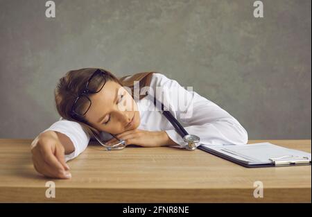 Infermiera giovane stanca o medico che dormiva seduto alla scrivania dell'ufficio dopo un lungo turno notturno Foto Stock