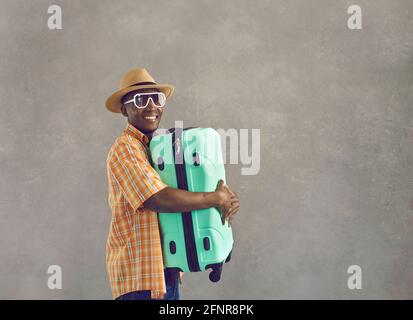 Ritratto dell'uomo africano felice in occhiali da sole e cappello da sole tenendo la valigia verde menta Foto Stock