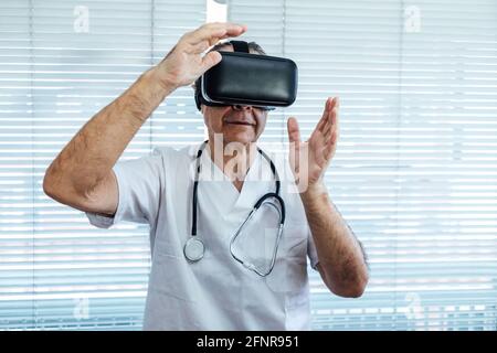 Dottore alla finestra di un ospedale, utilizzando occhiali di realtà virtuale per scopi medici, toccando qualcosa di virtuale con le mani Foto Stock