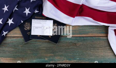Bandiera americana con covid 19 scheda di vaccinazione e US Passaporti su tavole rustiche in legno blu in dissolvenza per i requisiti di viaggio concetto Foto Stock