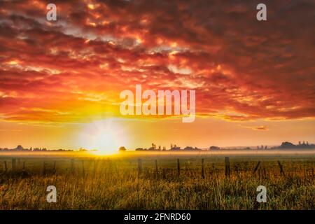 Stordimento delle nuvole colate all'alba sopra il pascolo agricolo rurale terreno agricolo con un po 'di nebbia e nebbia e. una forte luce solare Foto Stock