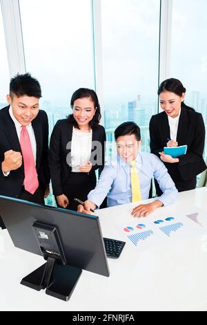 Gruppo di uomini d'affari che guardano al computer con grafico attivo la scrivania in ufficio Foto Stock