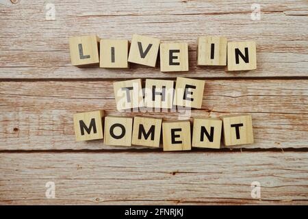 Lettera alfabetica Live in the Moment su sfondo di legno Foto Stock