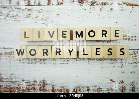 Vivi di più senza preoccupazioni lettere alfabetiche di Word su sfondo di legno Foto Stock