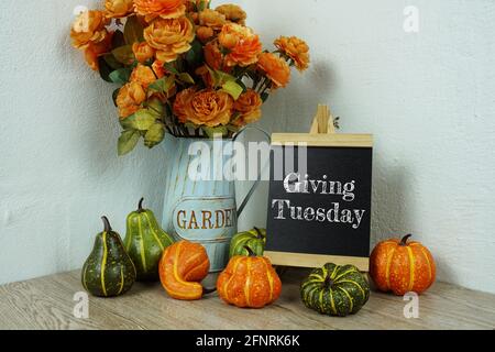 Dare il testo tipografico del martedì sul cavalletto a bordo con fiori artificiali e zucca sulla decorazione interna di un tavolo in legno Foto Stock