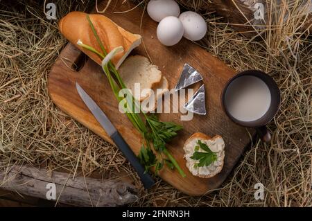 Colazione con uova sode e latte. Affettato pane e latte in una tazza. Tavola di legno e fieno. In alto. Foto Stock
