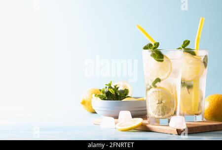 Due bicchieri con cocktail alla limonata o mojito con limone e menta, bevande rinfrescanti fredde o ghiaccio su sfondo blu. Spazio di copia. Foto Stock