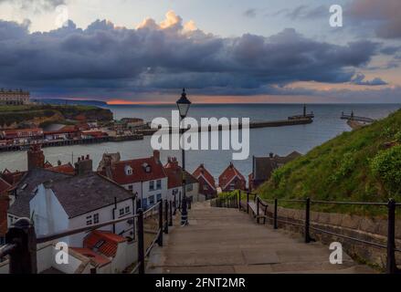 La vista dai famosi 199 gradini di Whitby. Preso come il sole tramonta creando una striscia rosa brillante all'orizzonte, guardando fuori sul porto. Foto Stock