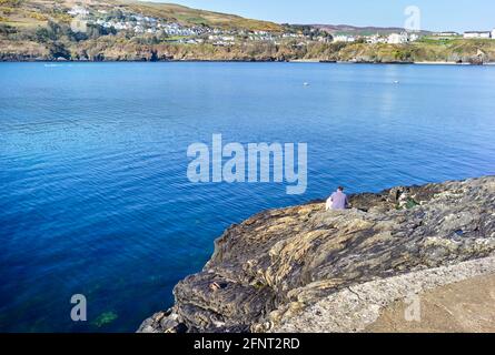 Un pescatore solista seduto su una roccia a Port Erin, Isola di Man Foto Stock