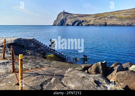 Tre subacquei che salono su scalini a Port Erin Isle Di uomo con testa di Bradda sullo sfondo Foto Stock