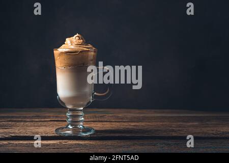 Caffè Dalgona in un alto vetro trasparente su sfondo marrone tinta. Vista laterale, spazio di copia. Foto Stock