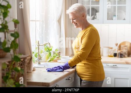 Buona-osservare la cucina anziana di pulizia della signora, indossando i guanti di gomma Foto Stock