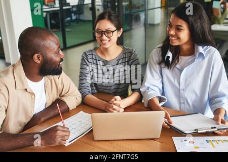 Tre colleghi d'ufficio amichevoli che si comunicano tra loro al lavoro Foto Stock