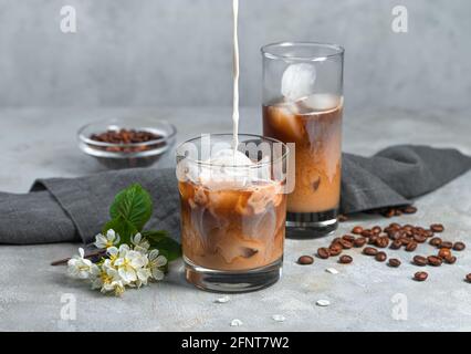 Caffè con latte e ghiaccio su sfondo grigio. Versare il latte in un bicchiere di caffè ghiacciato. Foto Stock