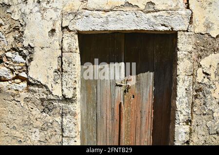 Vecchia facciata casa rurale abbandonata con un muro di pietra intemperie e una porta in legno antico ad Aroniadika un villaggio tradizionale di Kythira isola, Grecia. Foto Stock