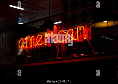 Incandescente Néon segno rosso AMERICANO e luci sfocate su sfondo nero. Immagine vintage con toni scuri. Foto Stock