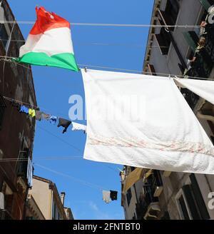 Molti vestiti appesi ad asciugare e il grande italiano Bandiera in un vicolo stretto in una calda giornata estiva senza persone Foto Stock