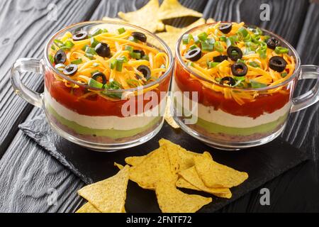 Delizioso antipasto cibo messicano a sette strati insalata di immersione servita con patatine primo piano sul tavolo. Orizzontale Foto Stock