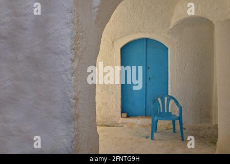 Casa rurale in legno blu chiaro porta ad arco su un muro stagionato bianco e una sedia di plastica blu chiaro in Mylopotamos Kythira isola Attica Grecia. Foto Stock