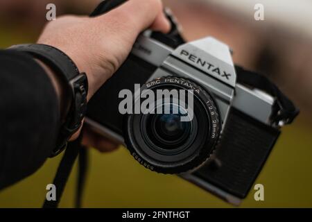 Mano del fotografo che tiene in mano una fotocamera da film d'epoca PENTAX K1000 in natura. Foto Stock