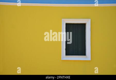 Finestra casa neoclassica con persiane di legno verde scuro e finiture bianche su una parete di colore giallo chiaro a Perlegkianika, isola di Kythira Attica, Grecia. Foto Stock