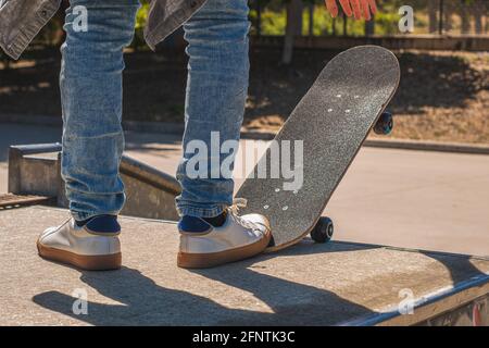 Dettaglio dei piedi di uno skater adolescente irriconoscibile che si prepara a scendere un ostacolo nel parco dello skateboard con il suo skateboard. Foto Stock