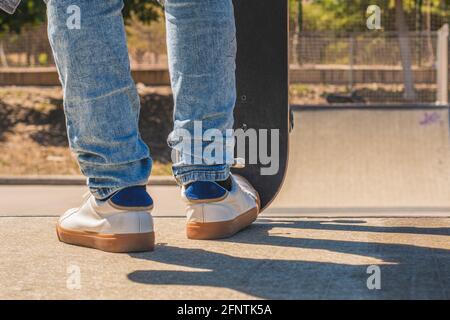 Dettaglio dei piedi di uno skater adolescente irriconoscibile che si prepara a scendere un ostacolo nel parco dello skateboard con il suo skateboard. Foto Stock