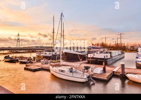 Yacht contemporanei e navi che galleggiano vicino al molo sull'acqua di canale contro il cielo nuvoloso tramonto in porto Foto Stock