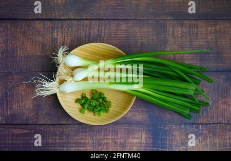Cipolle intere con radici e cipolle tagliate su un piatto di bambù. Foto Stock