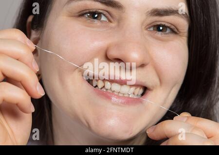 Una donna bruna pennellerà i denti con il filo interdentale. Igiene orale, rimozione della placca e prevenzione della carie dentaria e infiammazione delle gengive. Odontoiatria Foto Stock