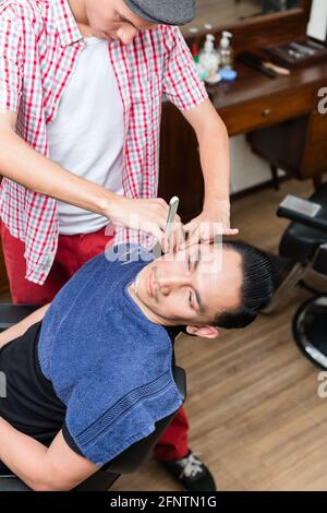 Uomo seduto su una sedia getting rasato con rasoio in Barberia Foto Stock