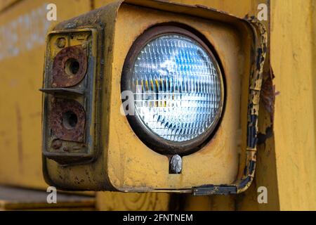 Faro di una vecchia macchina abbandonata per la costruzione di strade rotte (livellatrice). Metallo arrugginito, vetro rotto e resti di vernice vecchia. Foto Stock