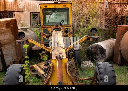 Vecchia macchina abbandonata per la costruzione di strade rotte (motorgrader giallo). Metallo arrugginito, vetro rotto, fari mancanti e residui di vecchia vernice gialla Foto Stock